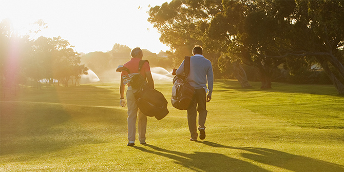 Two men walking on a golf course with golf bags at sunset.