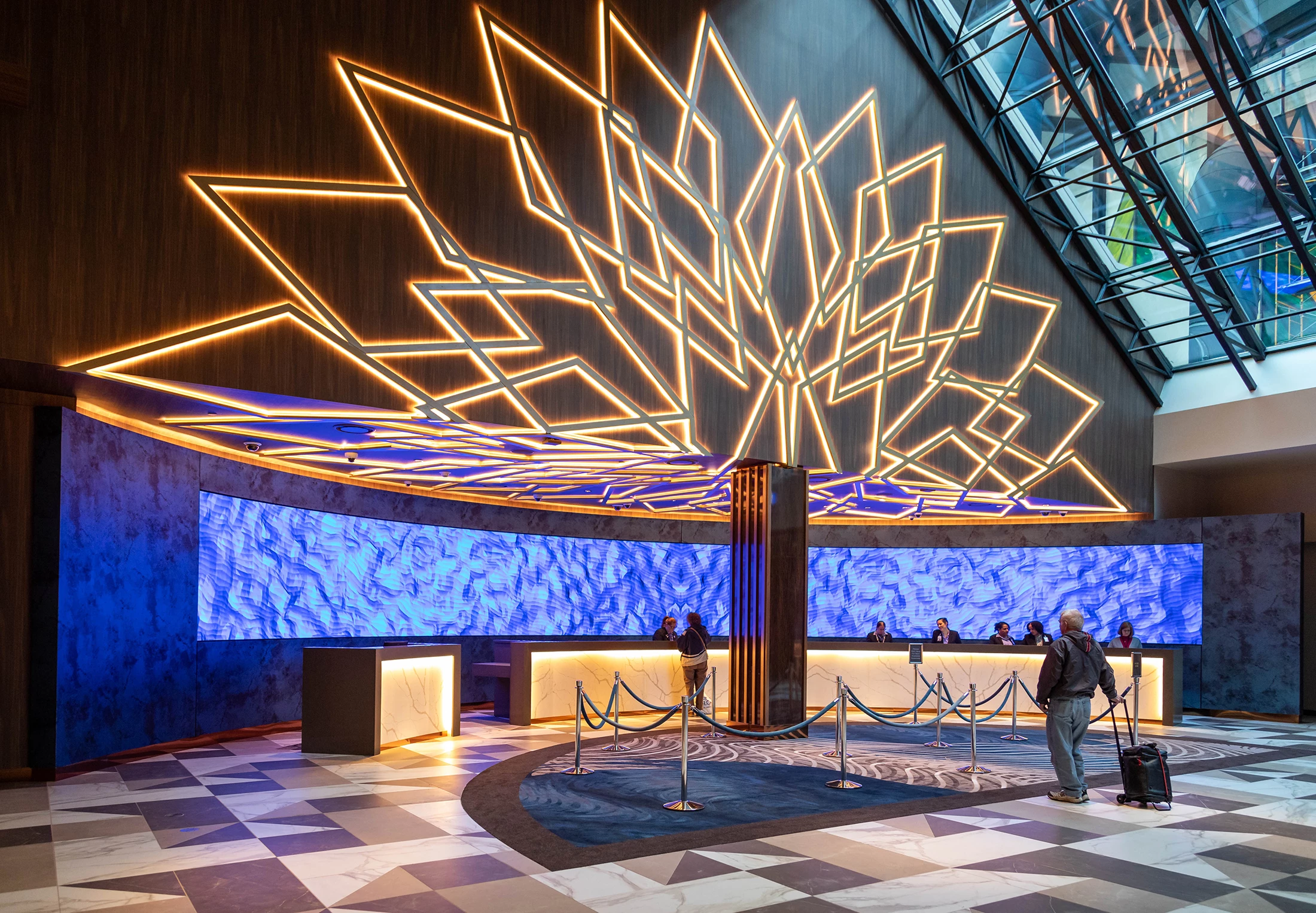 Hotel lobby check in desk with beautiful lighting installation and man with suitcase walking to the desk.