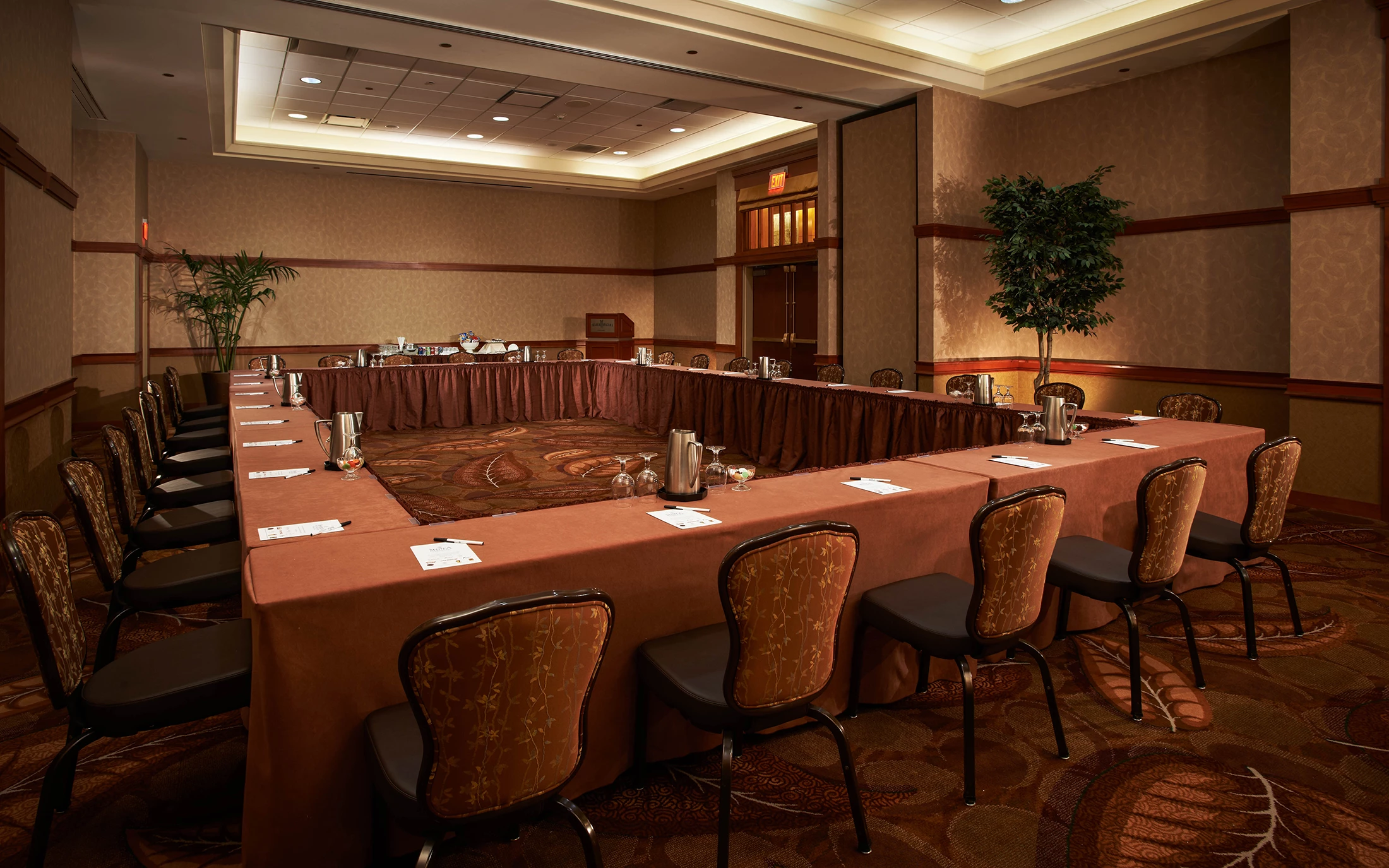 A meeting room with tables arranged in a rectangle with note pads in front of chairs.